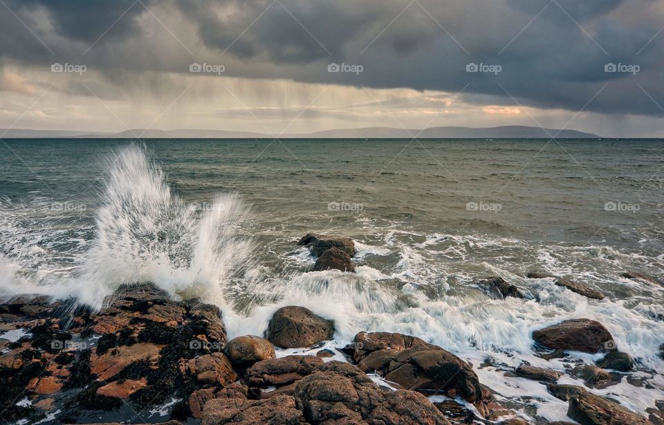 Dramatic cloudy seascape scenery with ocean waves splashing on rocky coast