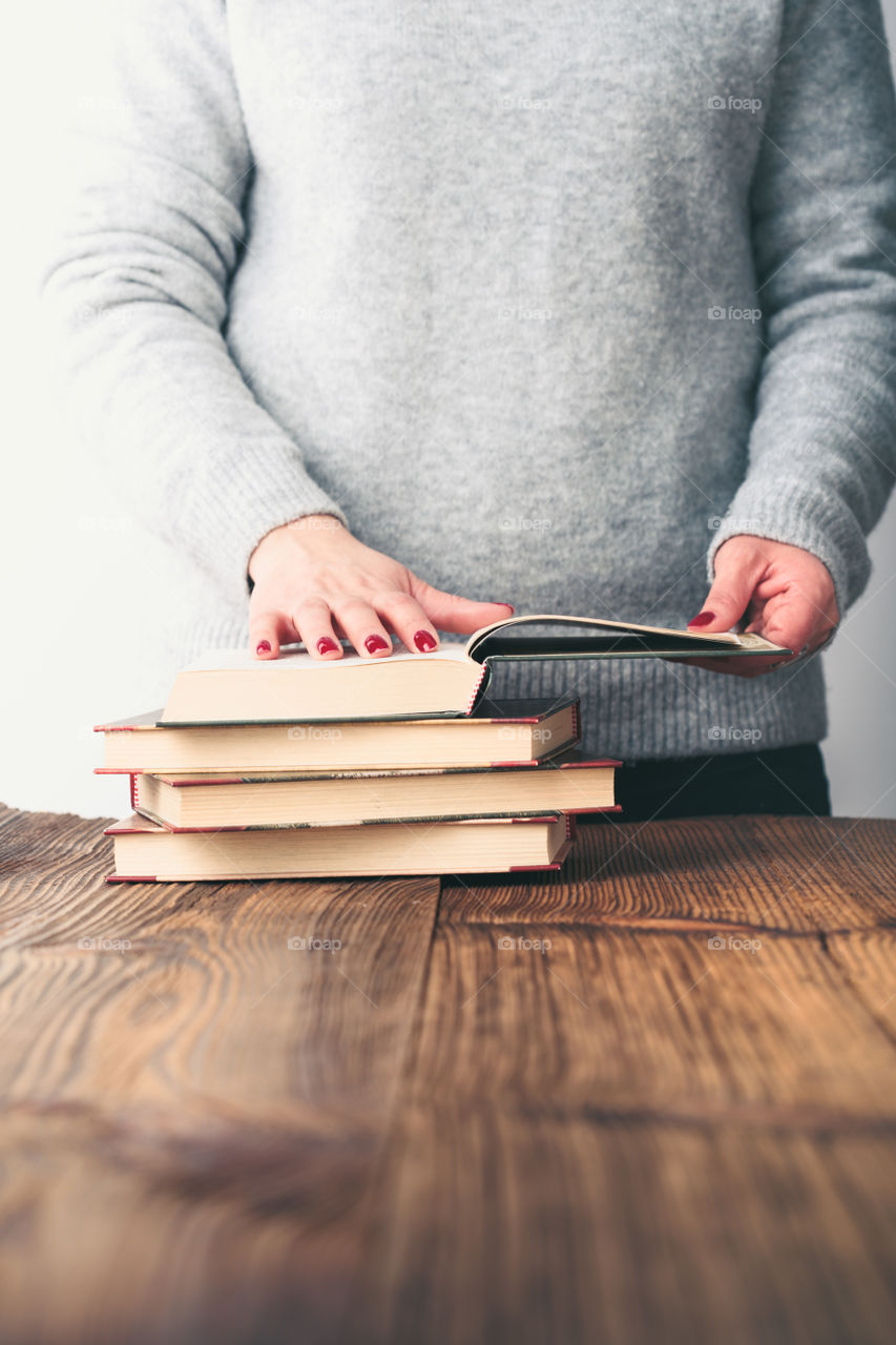 Young woman turning pages of old book on wooden table in antique bookstore. Woman wearing grey sweater and jeans. Vertical photo. Space for text