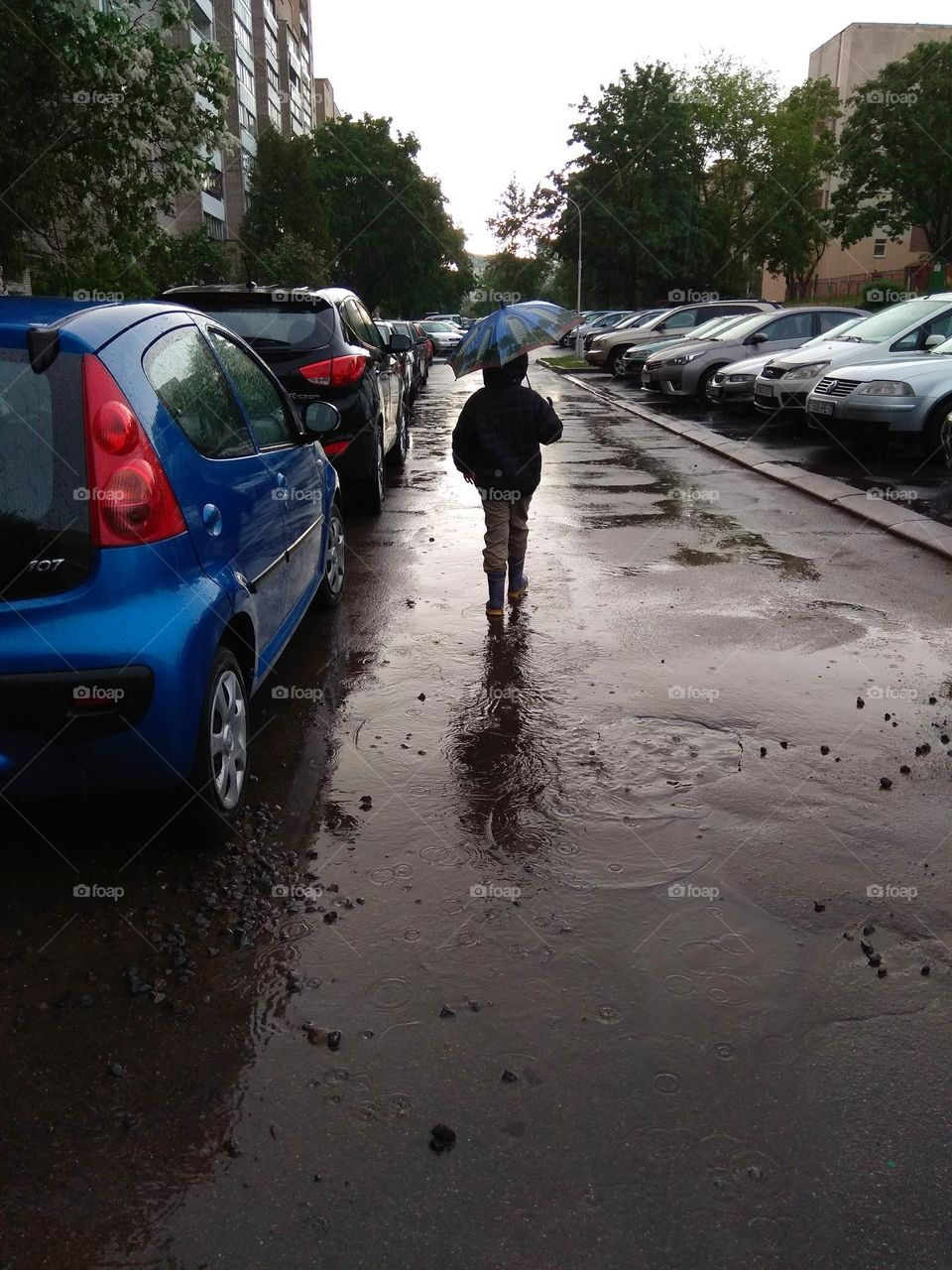 child walking on a street road with umbrella rainy day