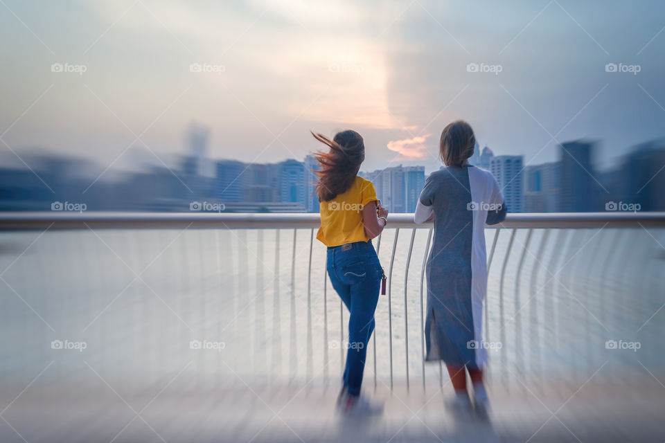 Two young women enjoying view of sunset city sky