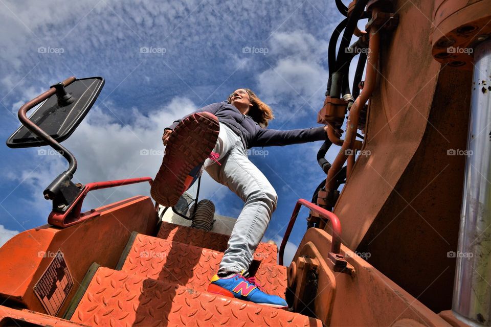 cool woman in jeans kicking foot on huge excavator wide angle frog perspective picture