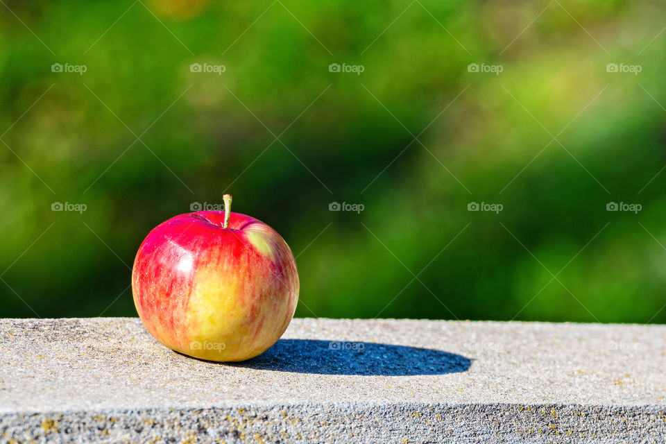 Lonely apple with shadow on a sunny day on the granite curbs. Selective focus. Blurred background.