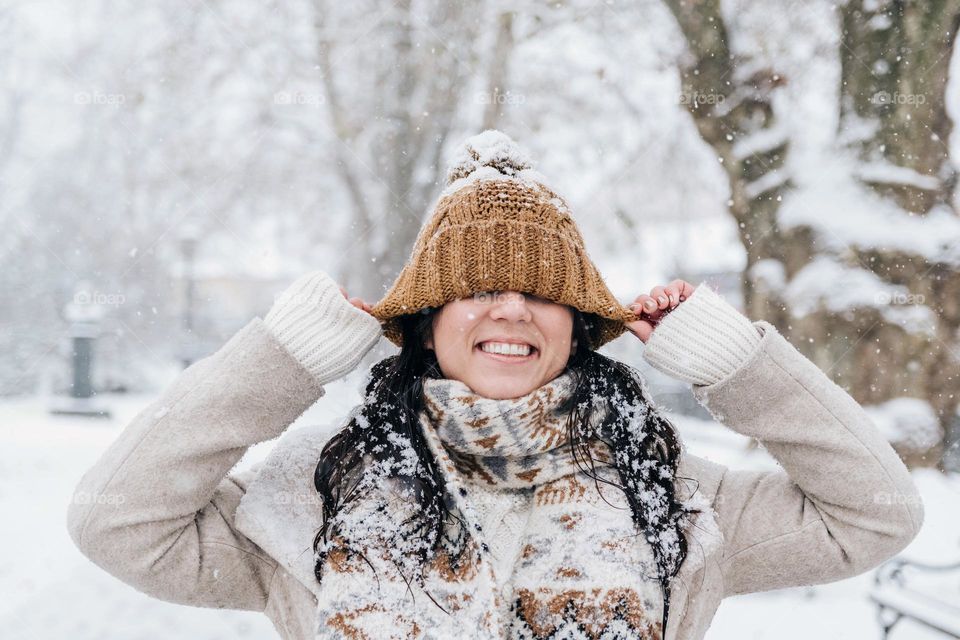 Portrait of happy young woman pulling her knit hat down over her eyes on a snowy day in winter