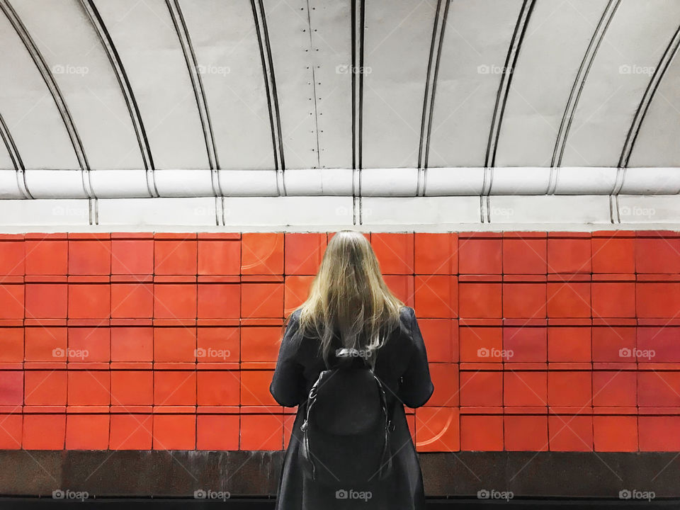 Young woman with long hair and backpack in front of the orange geometric wall background 