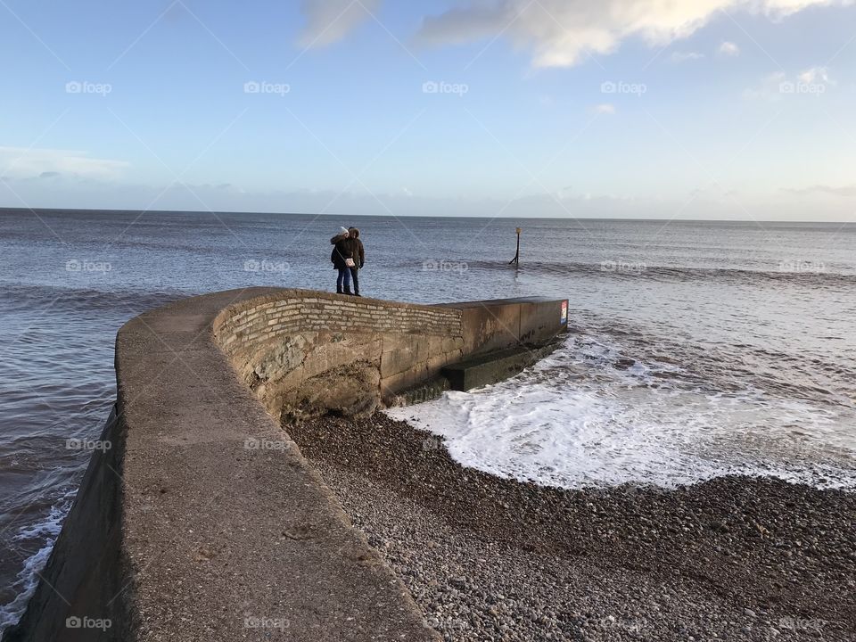 Landing strip with two people in distance mucking about despite the roaring sea.