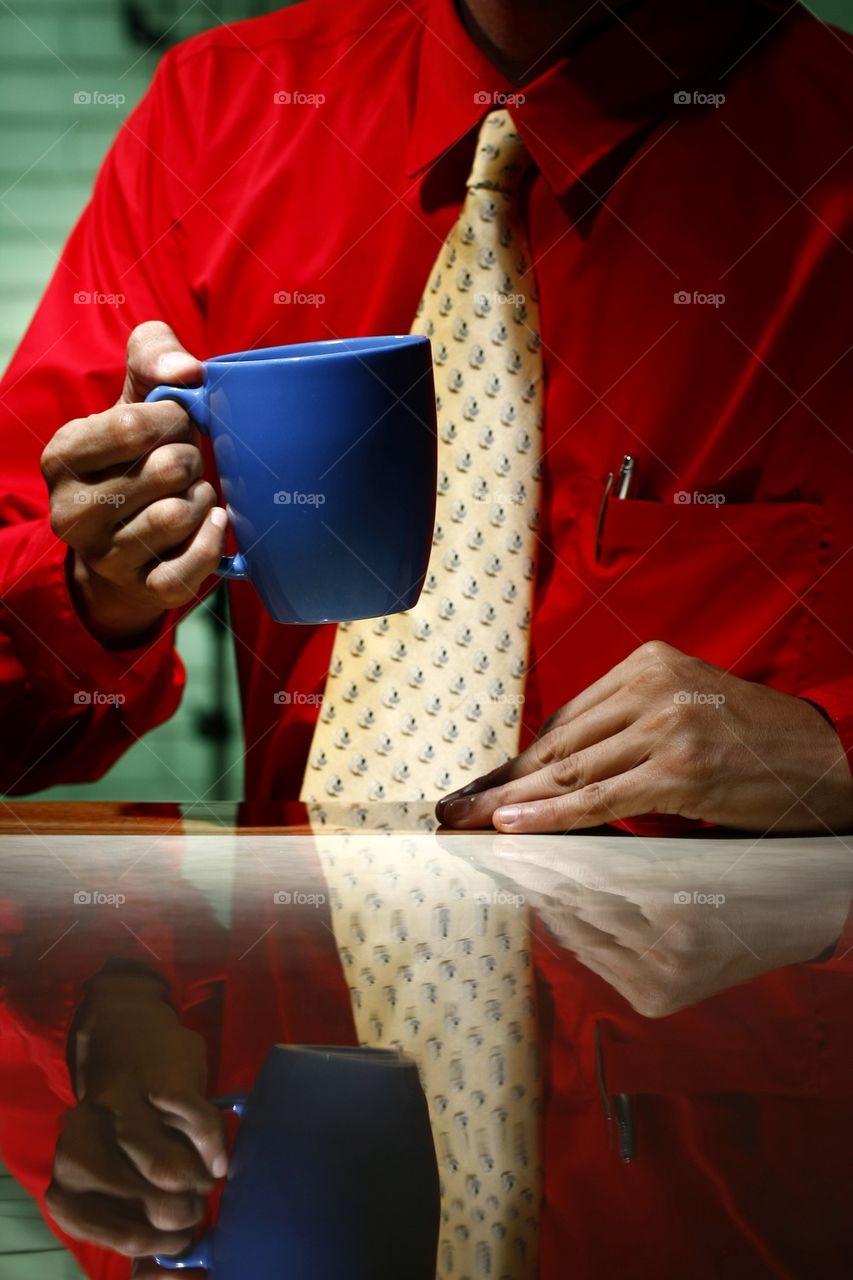 man wearing red shirt and yellow necktie holding blue coffee mug