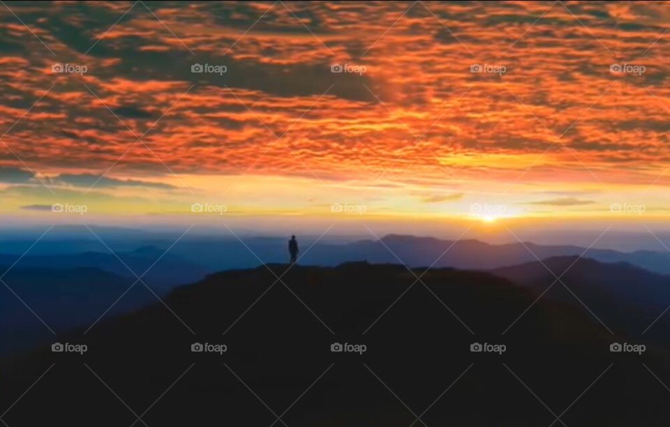 Natural world: single man on mountain with beautiful sunset and dark cloudy weather.