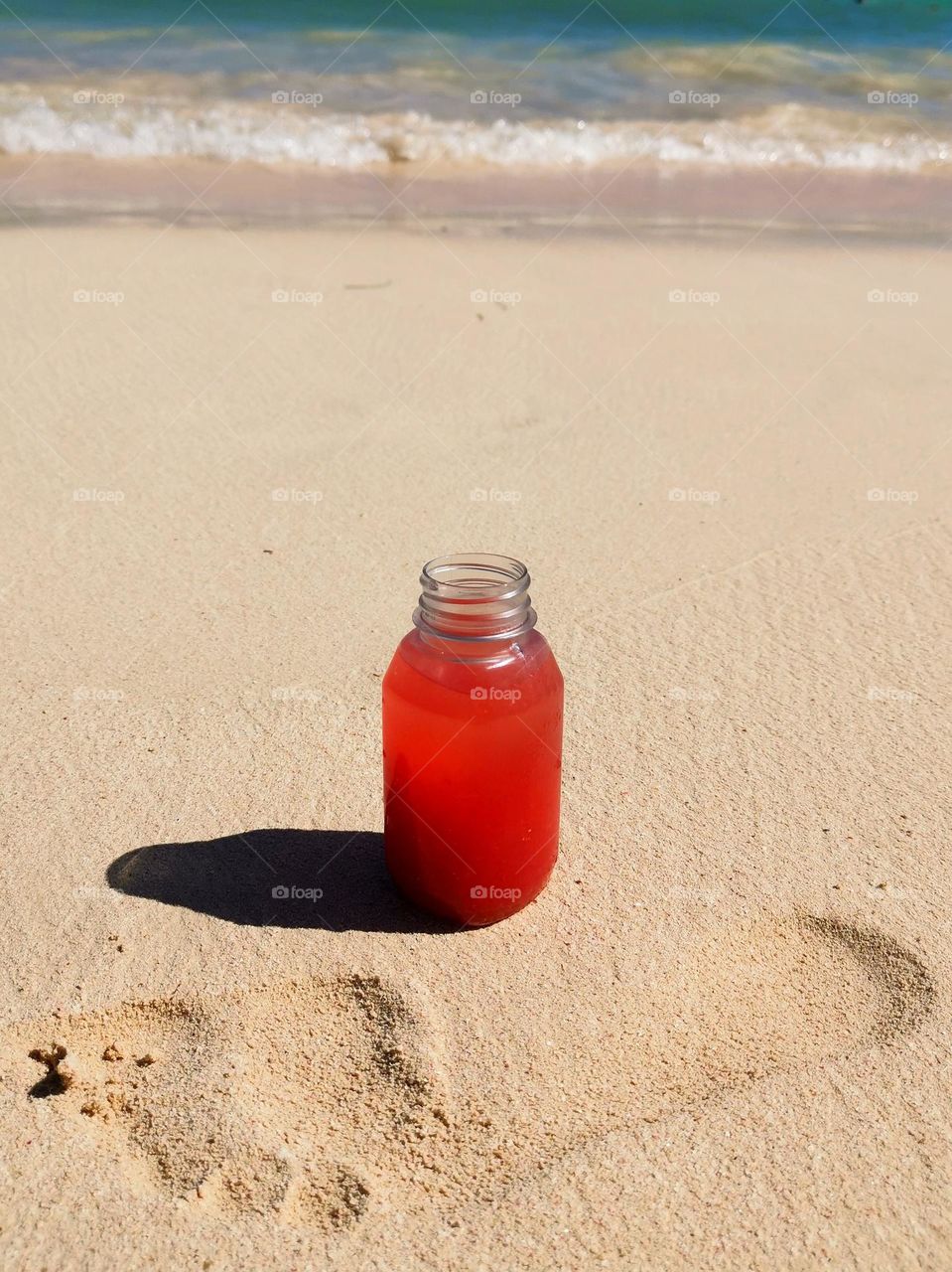 Seashore. Small bottle of juice on the sand. Footprint in the sand. Sunny day on the beach.
Unusual shooting angle. Shooting from below. Down up. From the ground up...