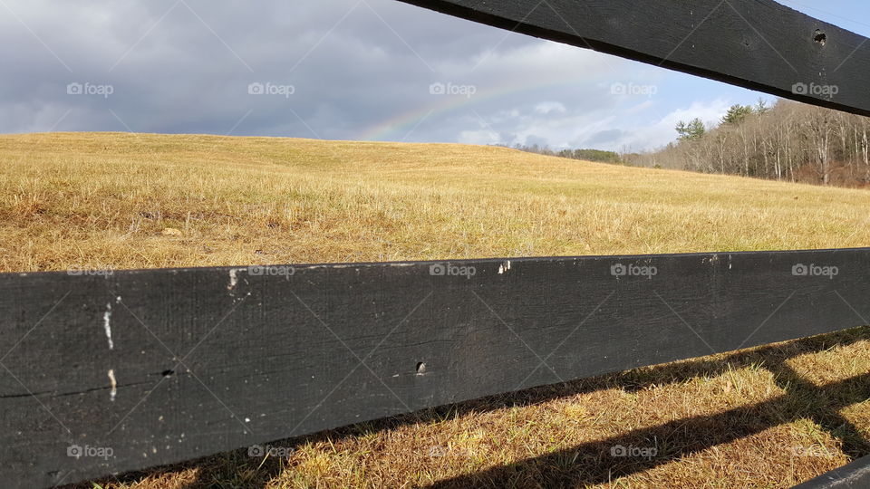 rainbow over a field with a simple fence