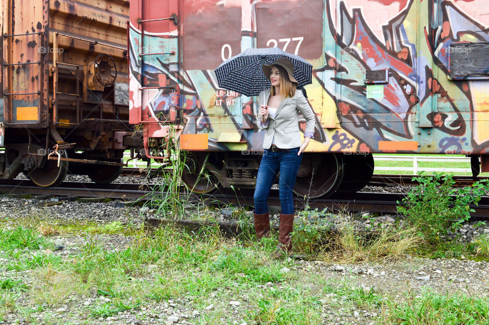 Woman standing in front of a colorful train car with an umbrella
