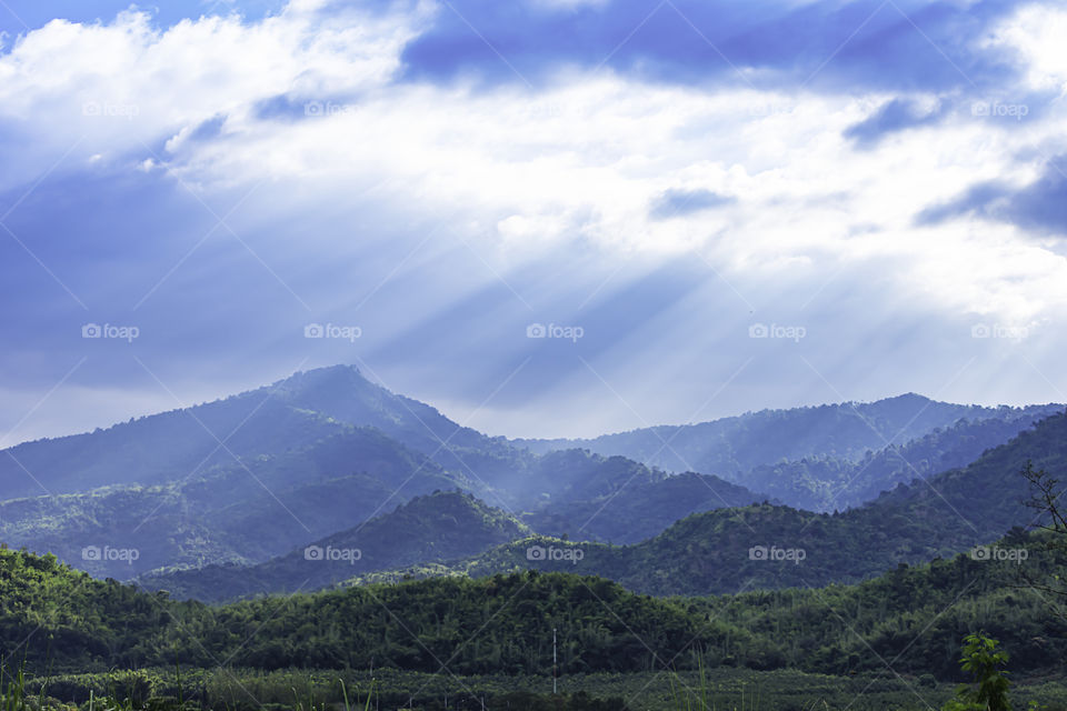 The sun shining through the clouds to the trees on the mountain at Suan phueng of Ratchaburi in Thailand.