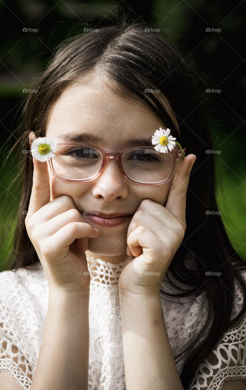 Portrait of a beautiful caucasian girl in glasses holding a camomile frame with a satisfied emotion on her face, close-up side view.