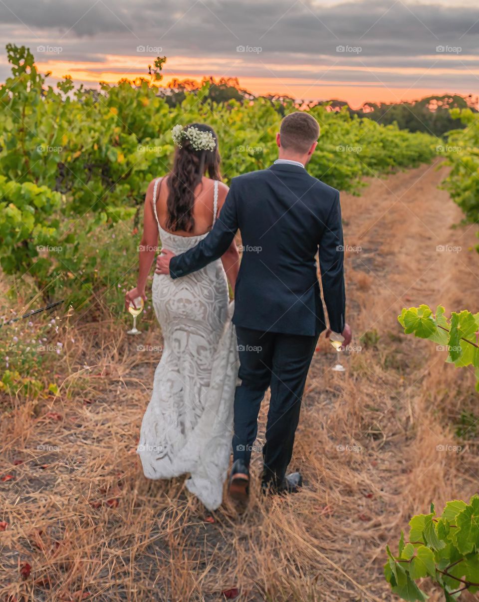 Bride and groom walk Into the sunset through a vinyard