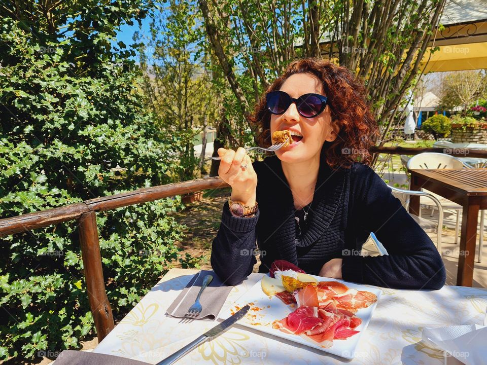 woman eats appetizer of salami and cheese in an outdoor restaurant