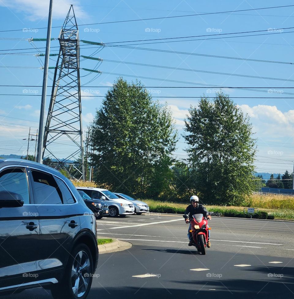 front facing view of a man riding a red motorcycle turning onto a street in Oregon on a sunny afternoon