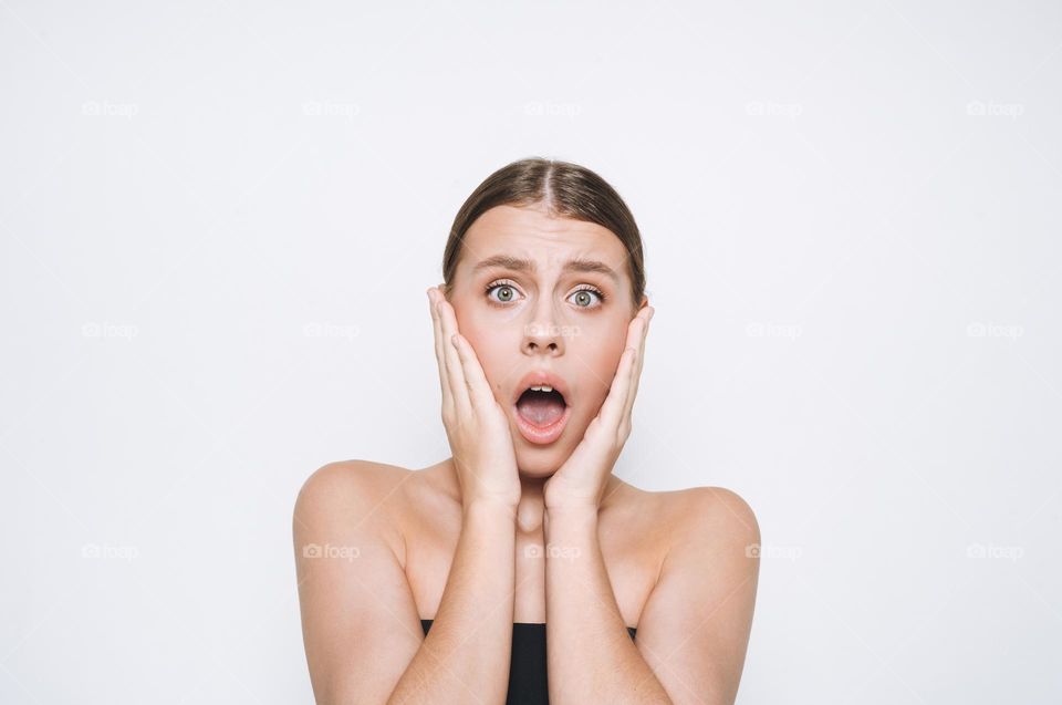 Portrait of surprised upset teenage girl frowns with hands near face on white background isolated