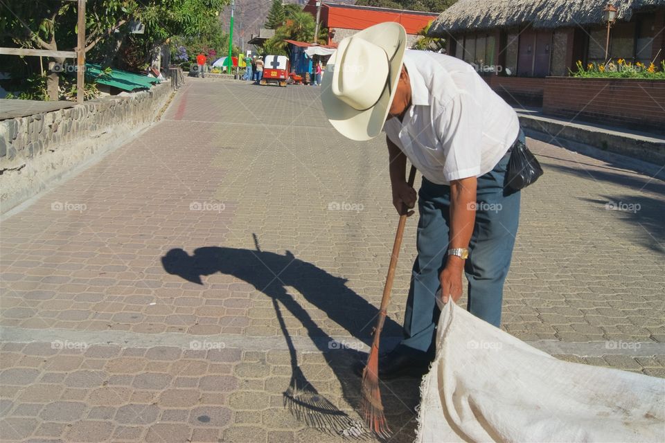 A man in Panajachel, Guatemala with a rake is sweeping debris into  a large canvass bag.