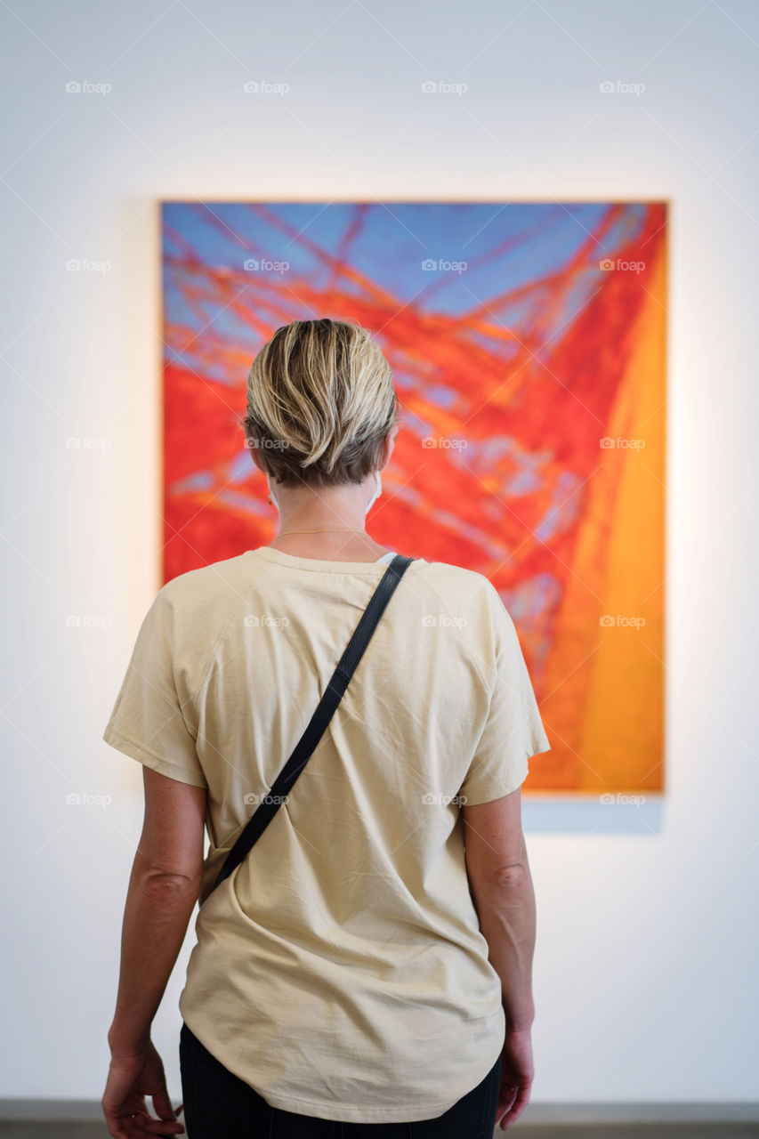 View from behind woman looking at the blue and orange abstract painting 
