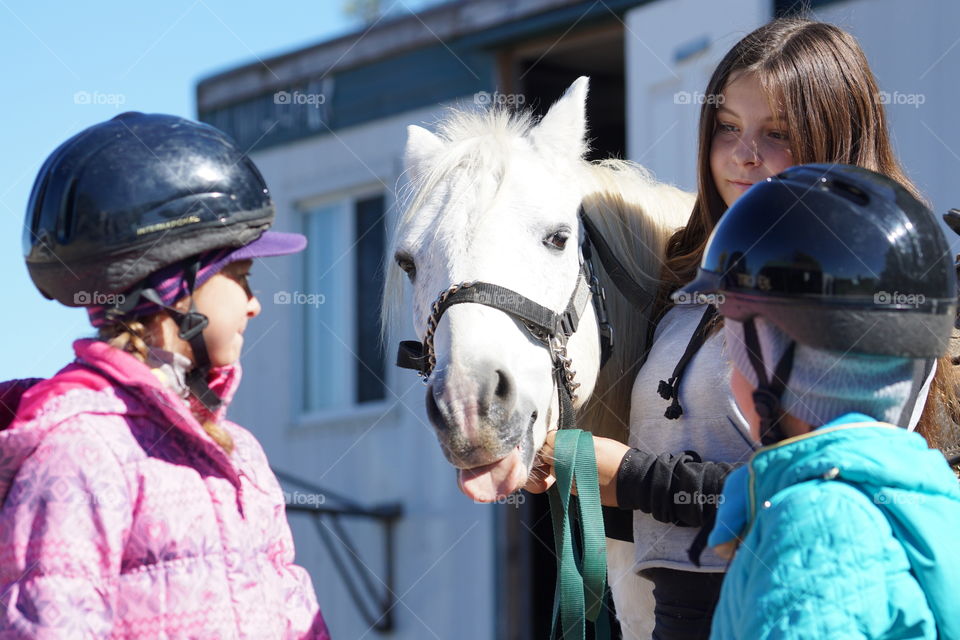 Girls standing with white horse wearing helmet