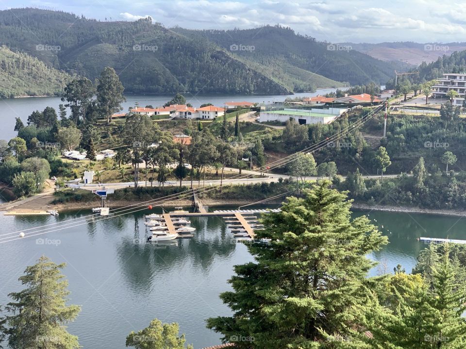 A view of Lago Azul, with a small harbour on the river, apartments and cafes, with tree covered hills in the distance