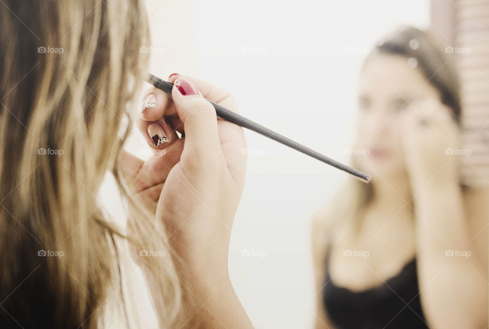 Woman in front of a mirror putting makeup on 