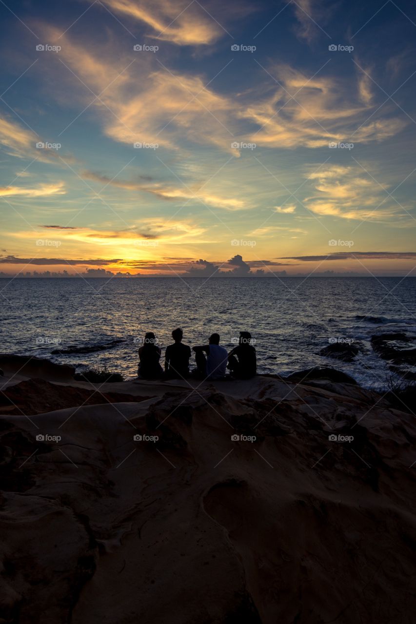 Four friends sat watching the sunset off of the cliffs of the Tip of Borneo, Borneo, Malaysia. 