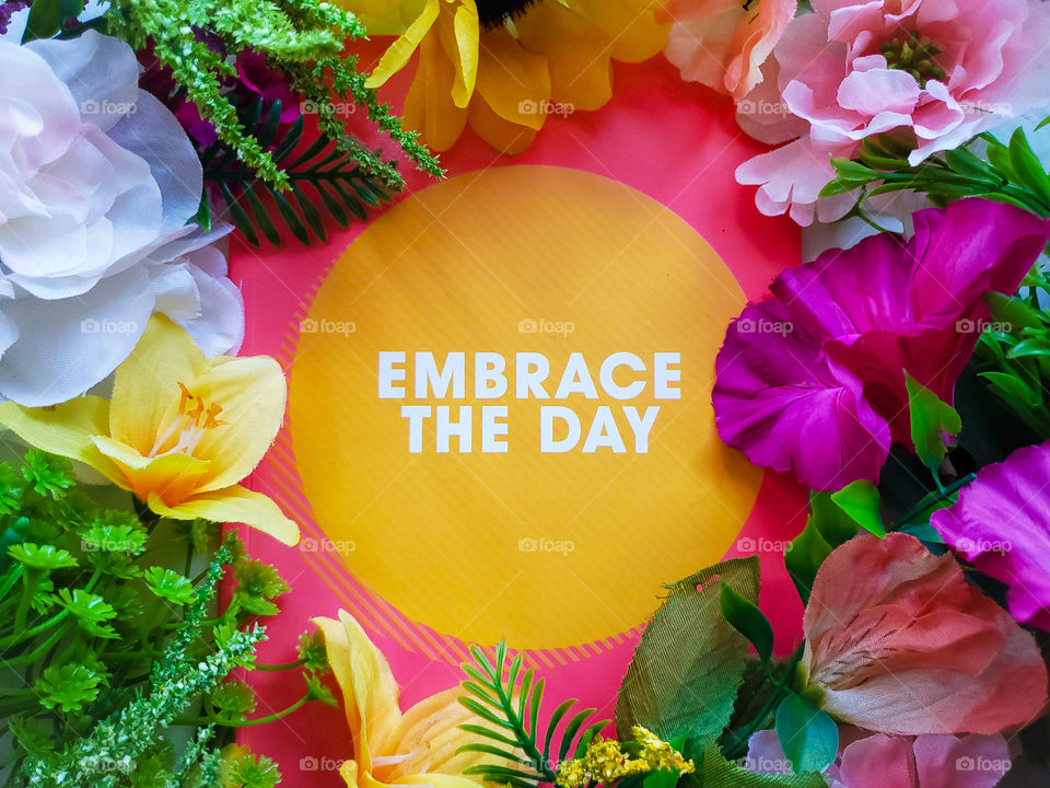 Colorful spring inspired flatlay with the motivational message Embrace the day , and surrounded by colorful flowers.