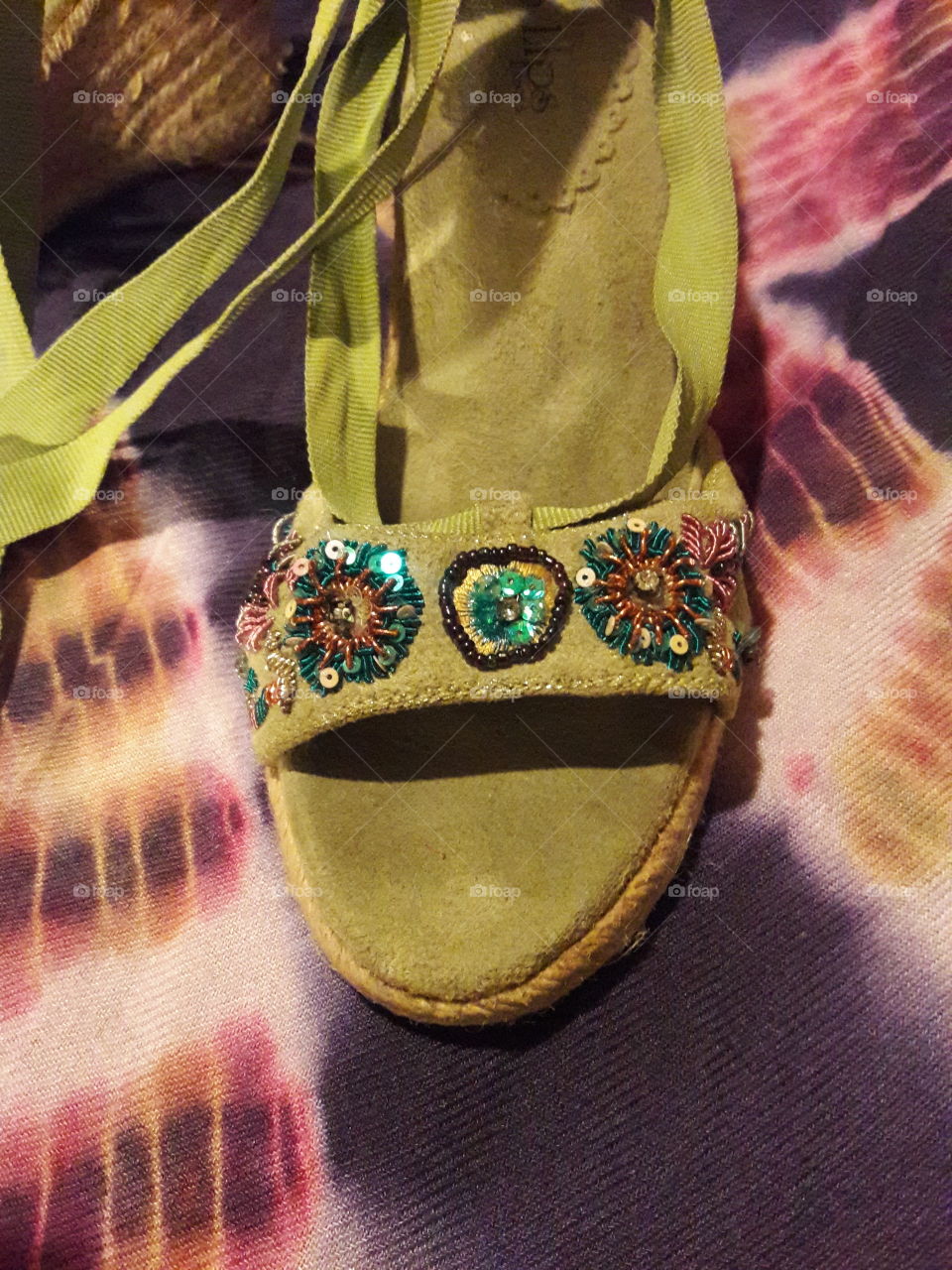 A close-up of the beadwork on a lime green suede wedge heel.