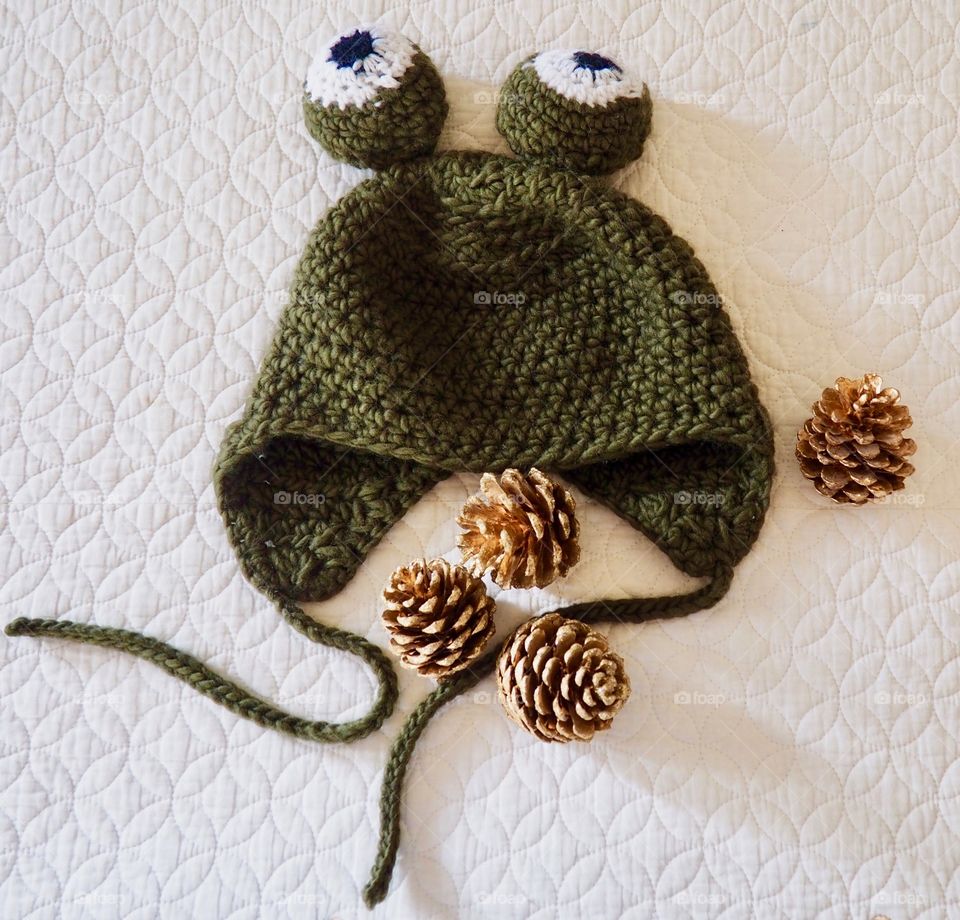 Child’s Green crochet frog hat with big round eyes.