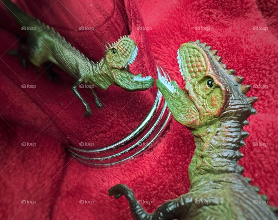 Toy dinosaur and its reflection in a silver cup on a red blanket