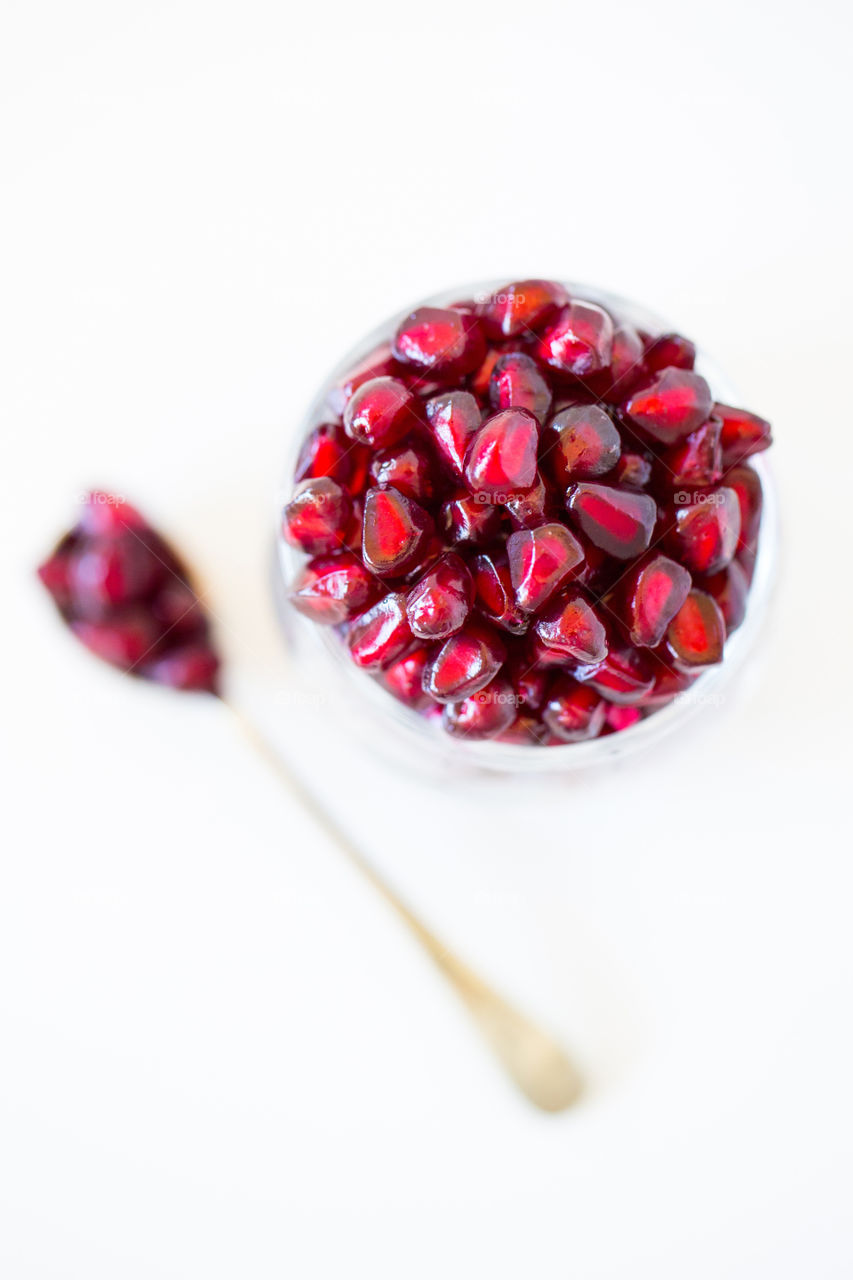 Closeup of red pomegranate seeds lay flat image from above. Red fresh summer fruit for nutrition and health. Minimalist image on a white background with single golden spoon.