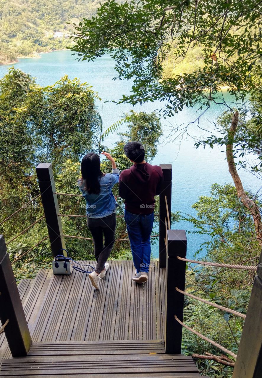 At the corner of forest walking trail, I met a couple were enjoying and talking, their posture and lake, sky, trees all were very beautiful. taking a walk of forest trail in holiday that is a good relaxing and leisure recreation.