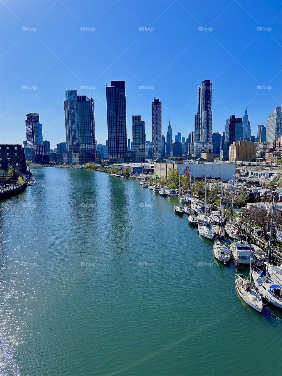 This is “Newtown Creek”, an ocean inlet of the “E River” seen from the “Pulaski Bridge” that connects LIC, Queens to “Greenpoint”, Bklyn. Across the water in the distance you see “Manhattan” incl. the “Empire State Bldg”. 2024. Hypnotic Productions