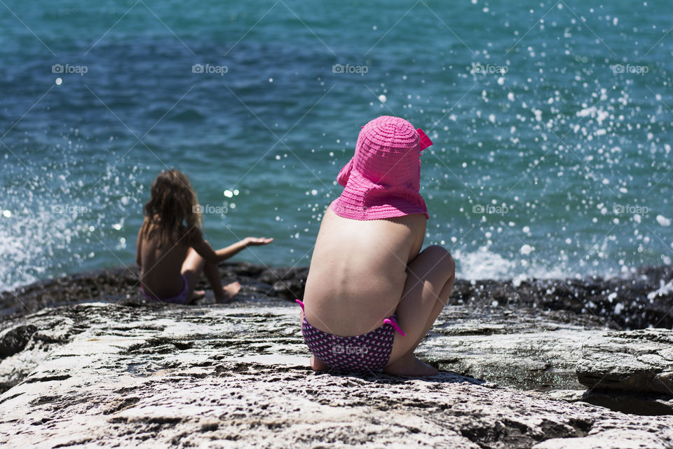 little girls on a beach. little girls watching waves splashing at rocks