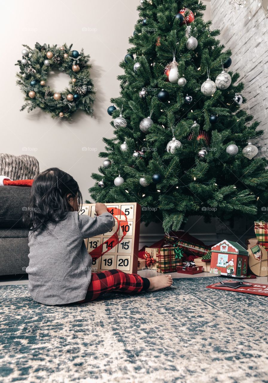A toddler sits facing the Christmas tree while opening and Advent Callander in the search of a treat.