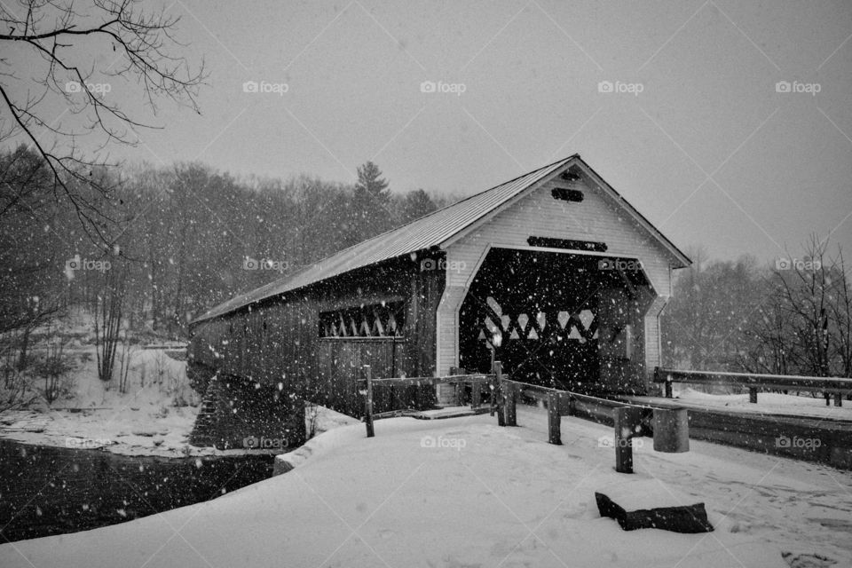 A covered bridge being blanketed with a soft layer of snow