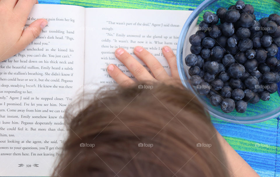 Child reading a book and snacking blueberries