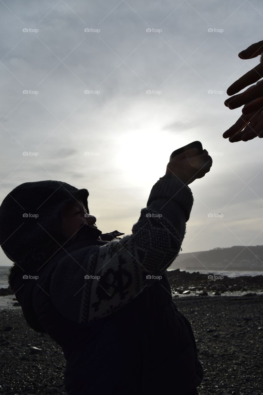 A  boy hands his father a rock from the beach as the sun rises 