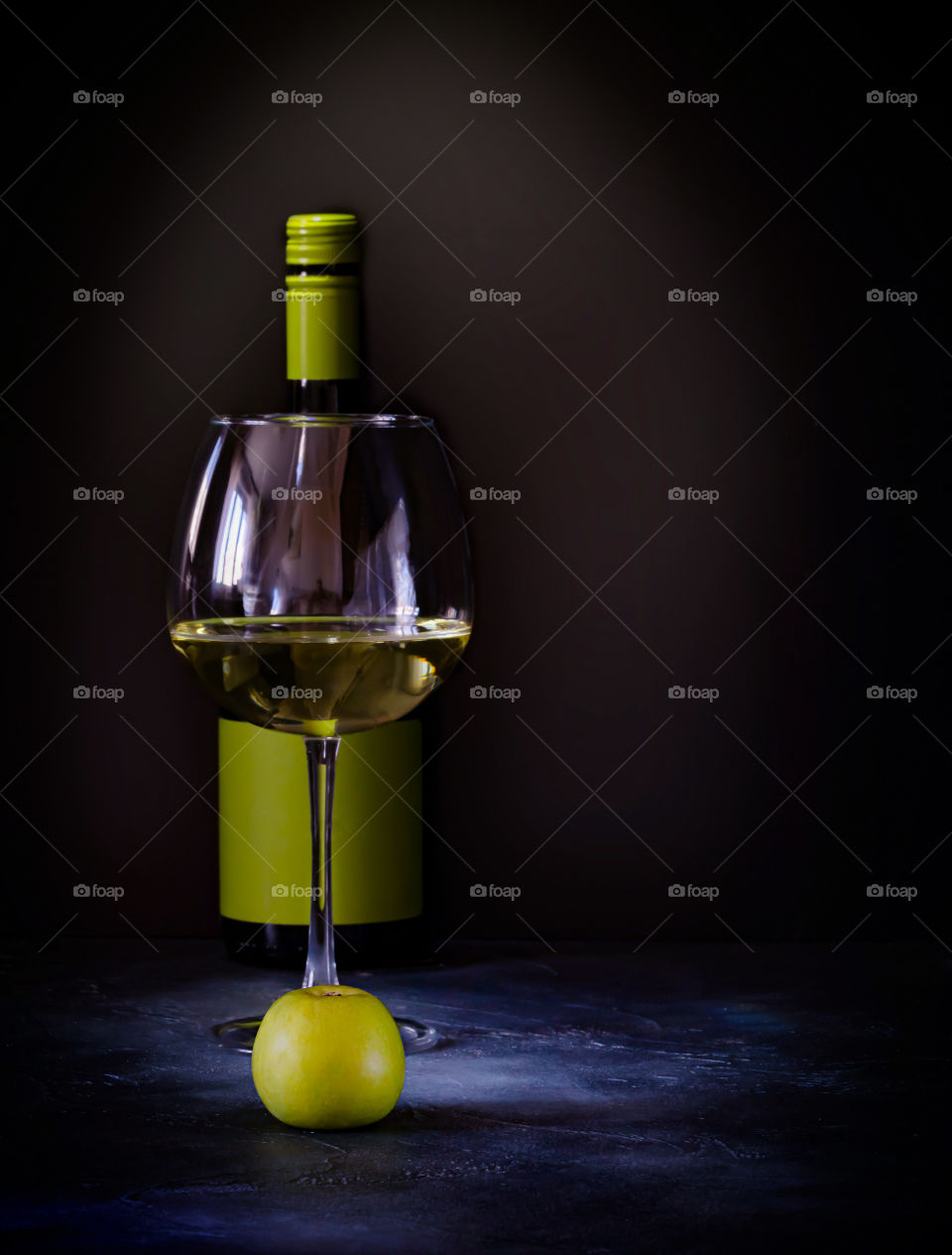Homemade apple wine.  A bottle, a glass of white fruit wine and an apple stand in front of each other on a dark background.  Food photo, vertical orientation, copy space