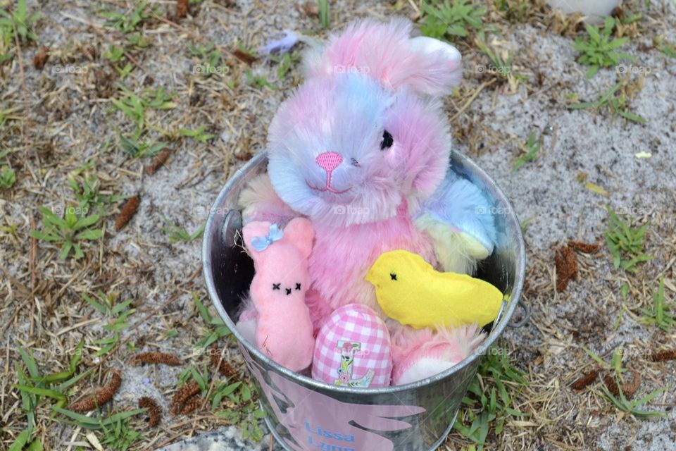 A silver bucket with a multi-colored pastel stuffed bunny holding a pink peep bunny, a pink checked egg, and a yellow peep chic