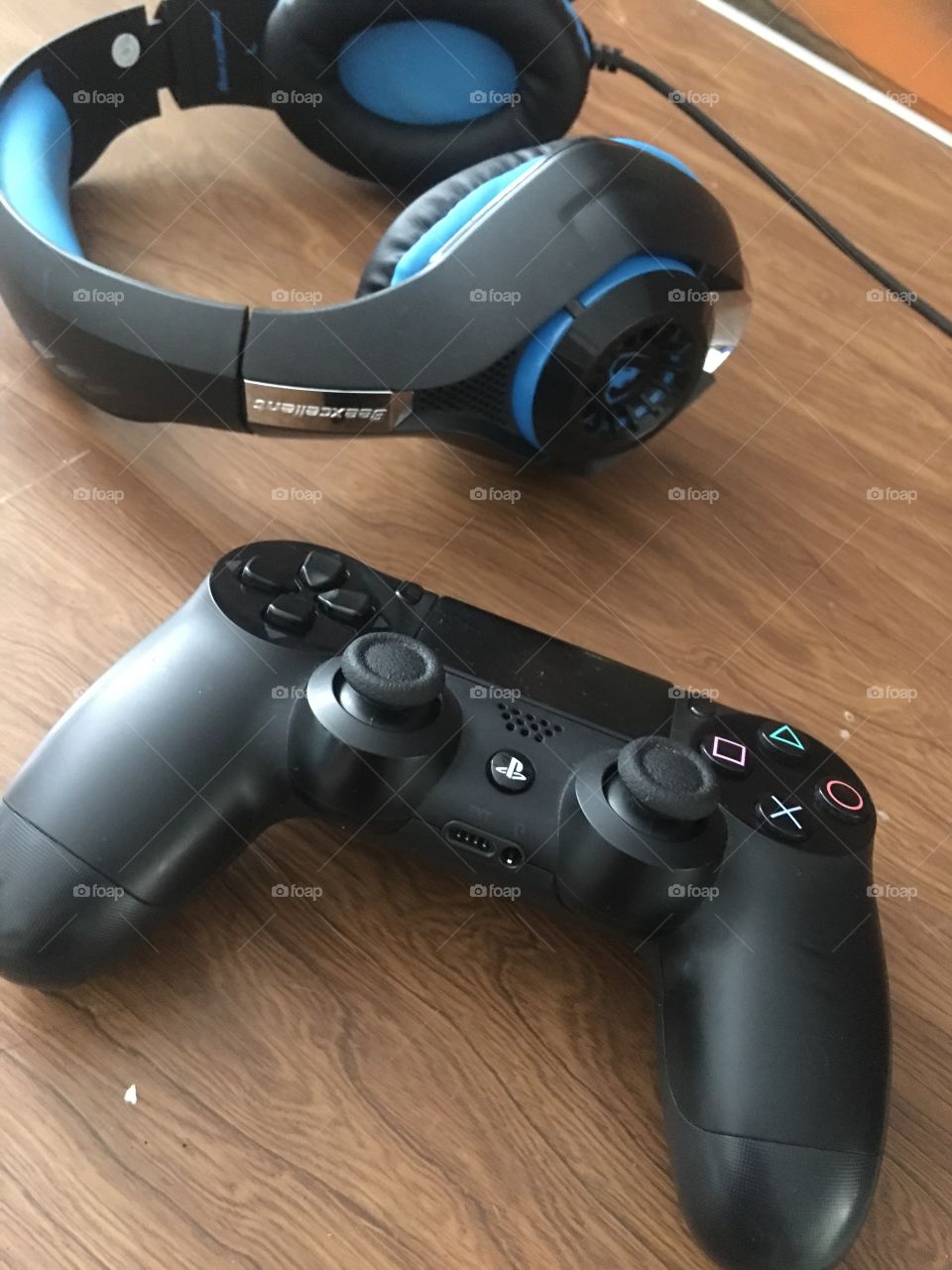 A PS4 controller and my blue and black gaming headset on a wooden table. Light coming from the left. 