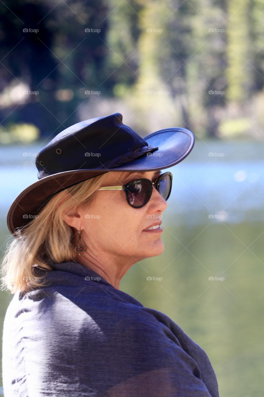 List in thought:  Profile headshot middle aged blonde haired woman wearing leather cowboy hat at sunglasses 