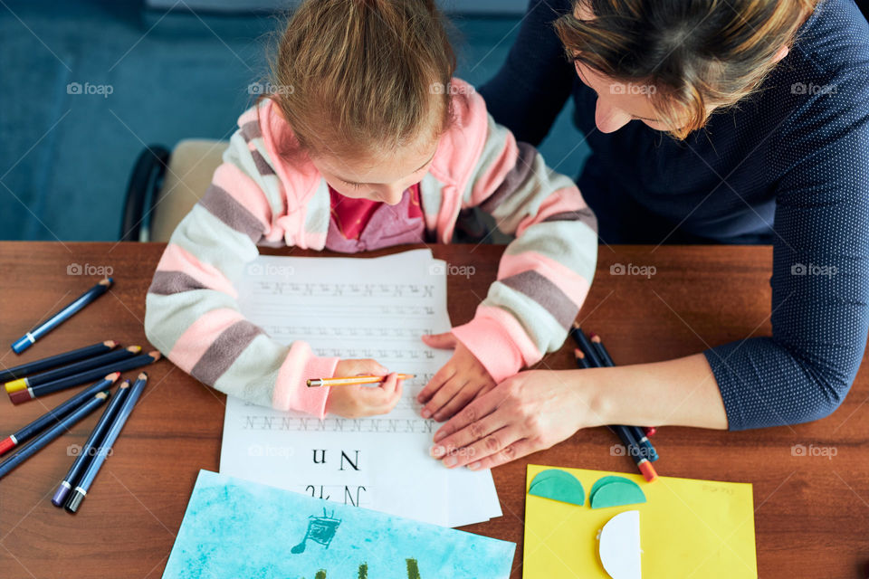 Little girl preschooler learning to write letters with help of her mother. Kid writing letters, drawing pictures, making stuff with paper, doing a homework. Concept of early education