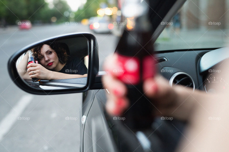 beautiful curly-haired girl, driving her car, drinking Coca-Cola, rejoicing, smiling