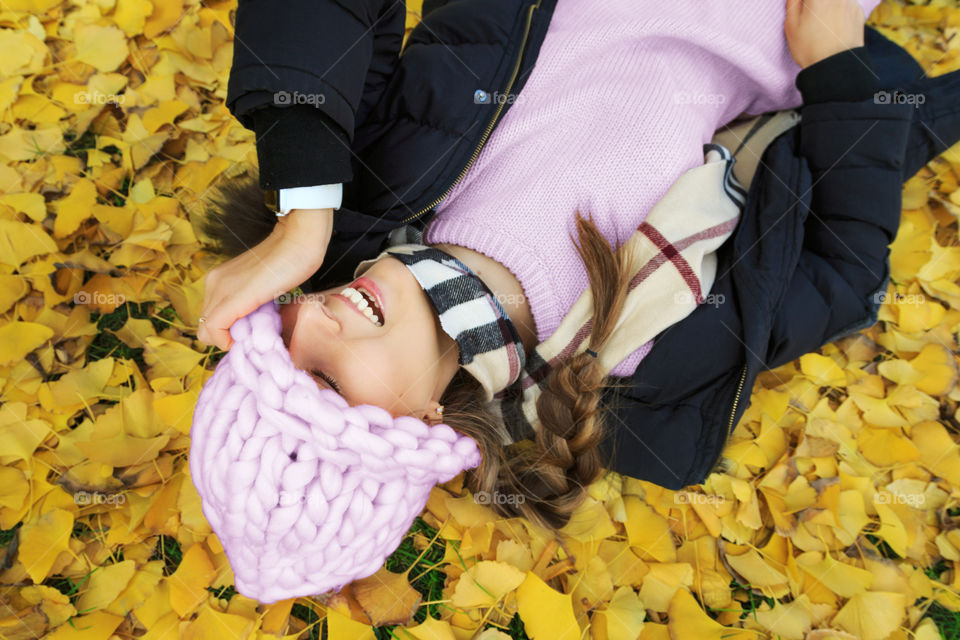 Happy woman lying on the ground with fallen yellow leaves 