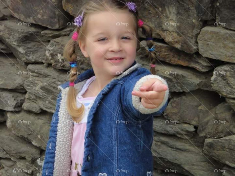 little girl pointing in front of stone wall