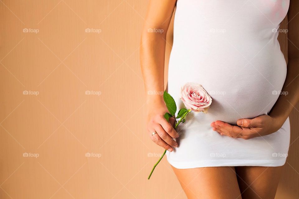 Mid section of pregnant woman holding rose