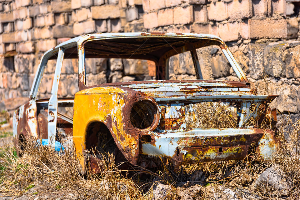 Abandoned and rusty skeleton of a Soviet Russian car growing hay inside by the side of the building exterior in Ararat province on 4 April 2017.
