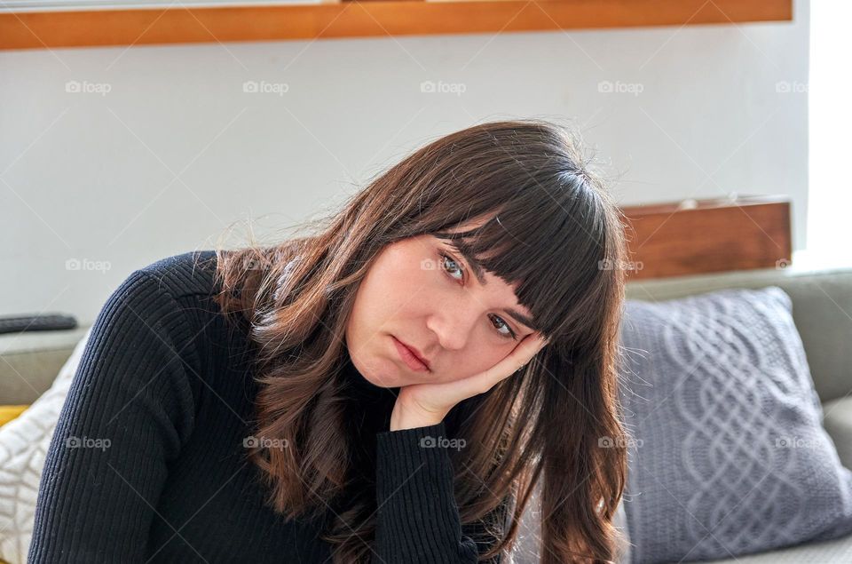 Sad girl sitting on sofa at home, leaning head on her hand