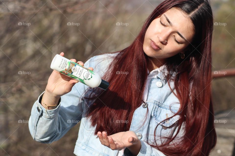 Pretty youn woman with long hair is using detangling solution by Herbal Essences